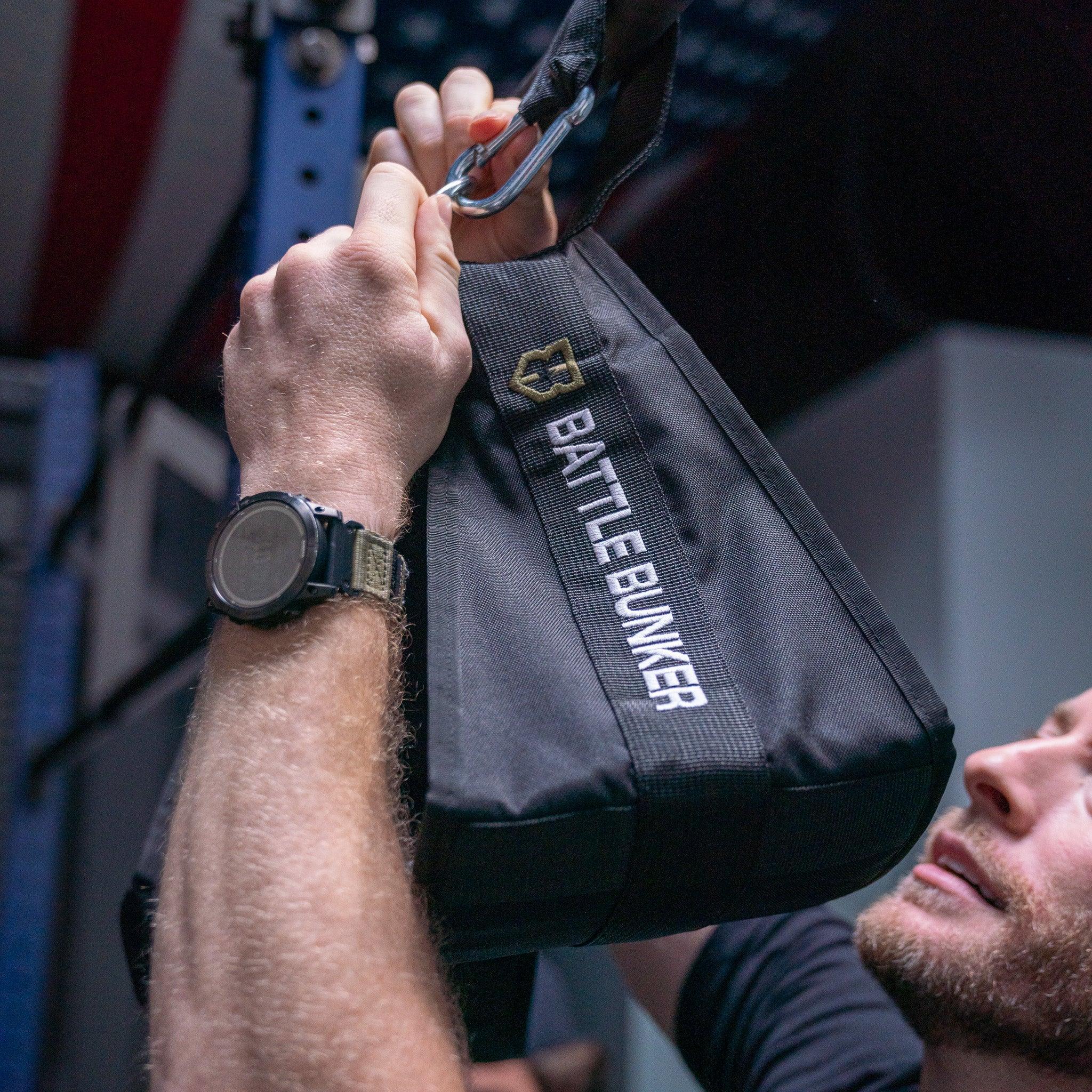 Man gripping black Battle Bunker gym strap with carabiner in close-up workout scene