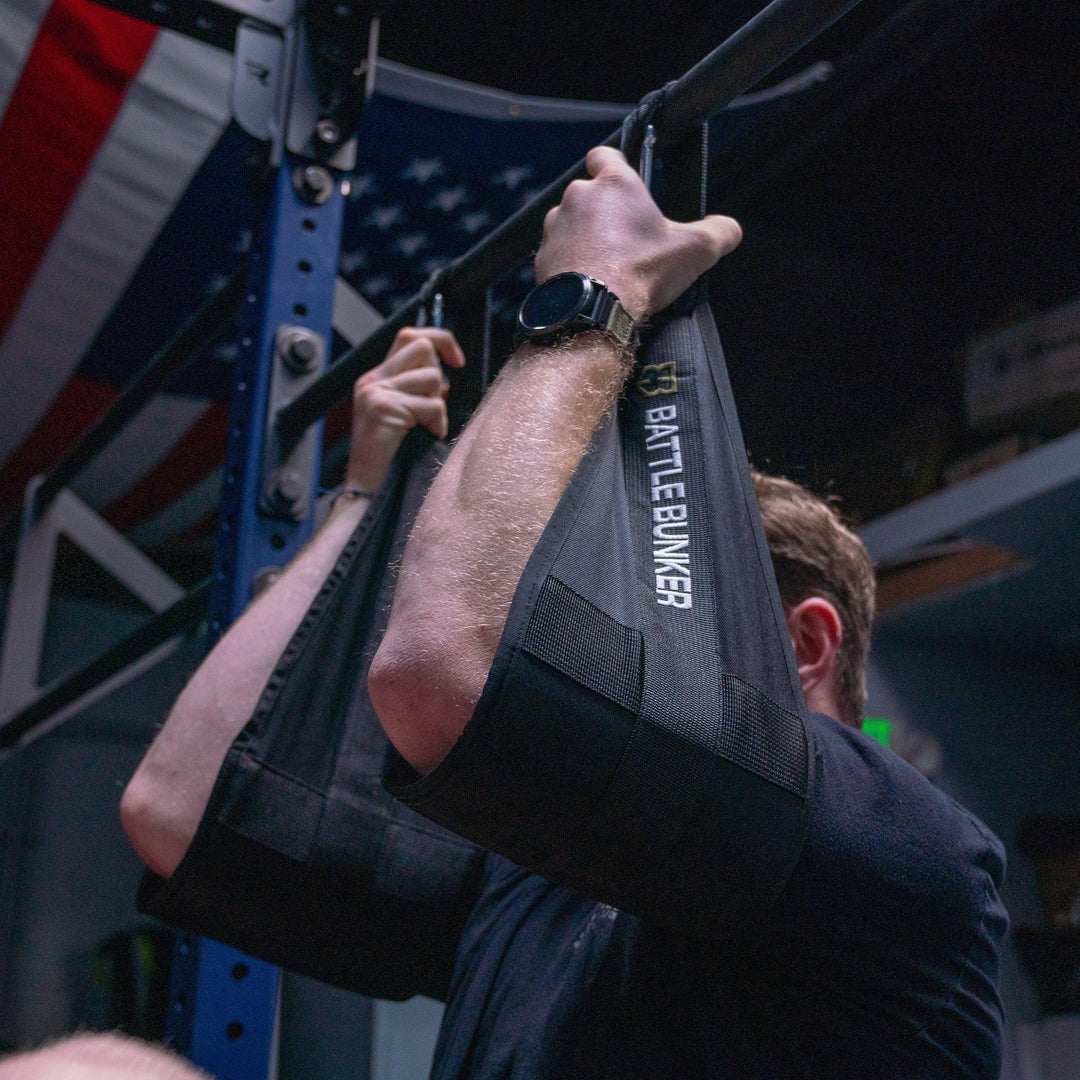 Person using Battle Bunker arm slings for assisted pull-up in a gym with American flag background
