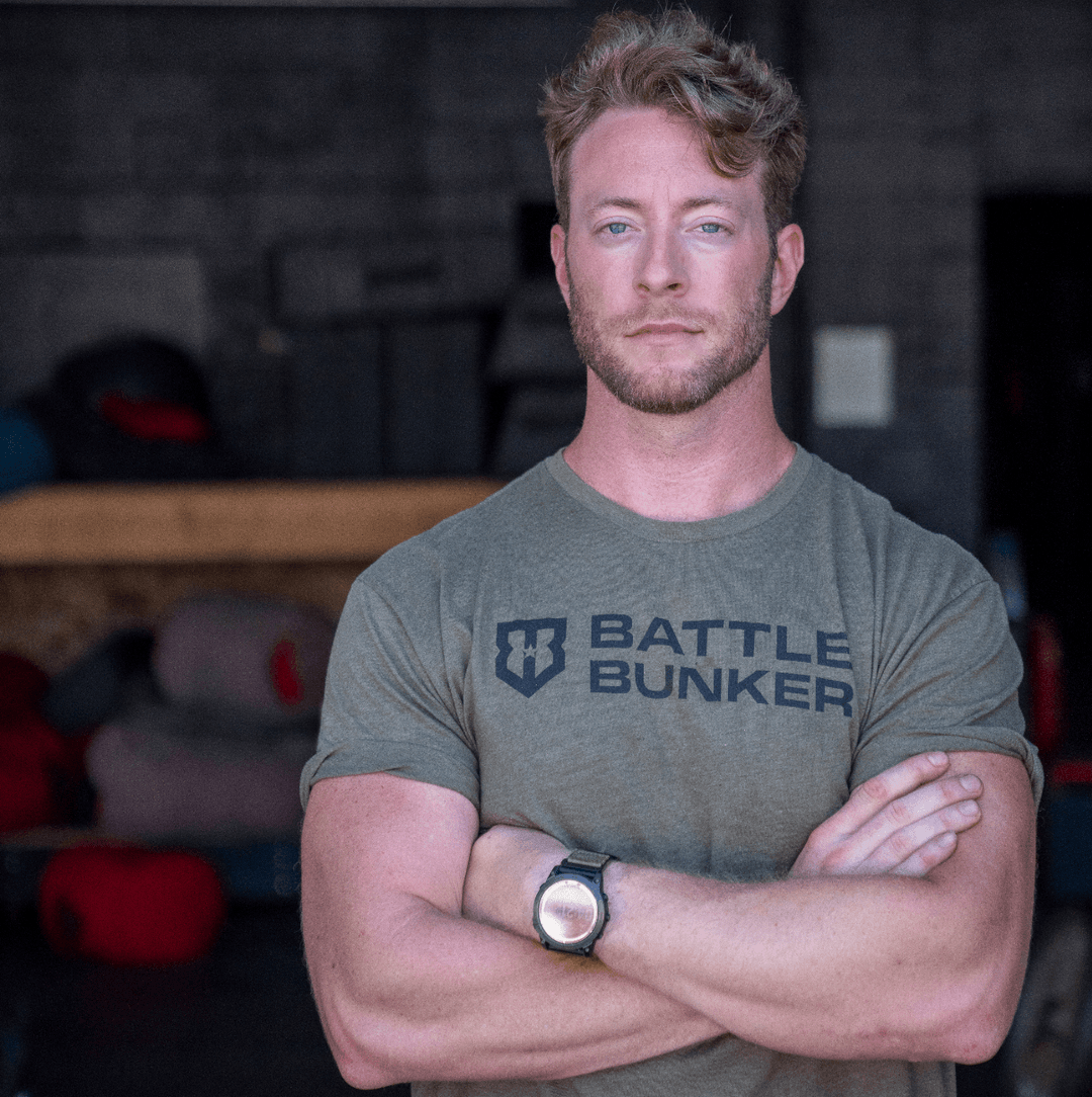 Fit man with crossed arms wearing a green Battle Bunker t-shirt in a gym setting