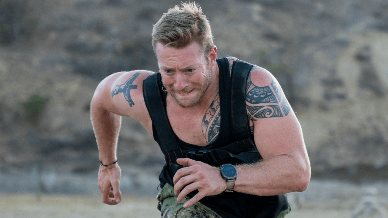 Man with tattoos sprinting outdoors wearing black weighted vest in Battle Bunker fitness training
