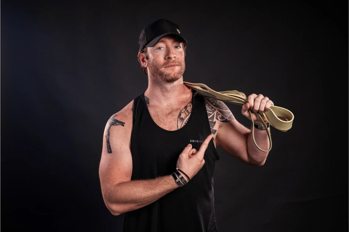Man wearing black tank top and cap holding and pointing to beige Battle Bunker resistance bands
