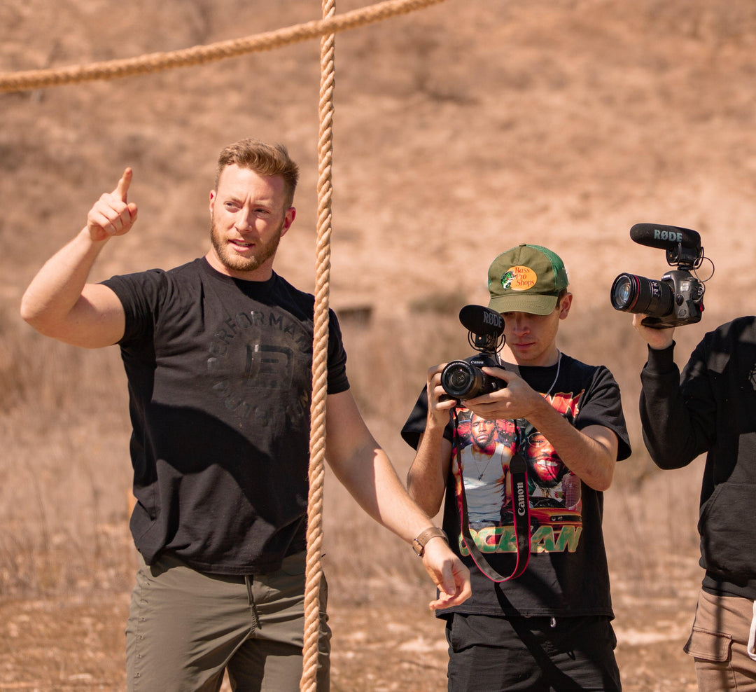 Man gesturing with finger while two cameramen film outdoors at battle bunker site