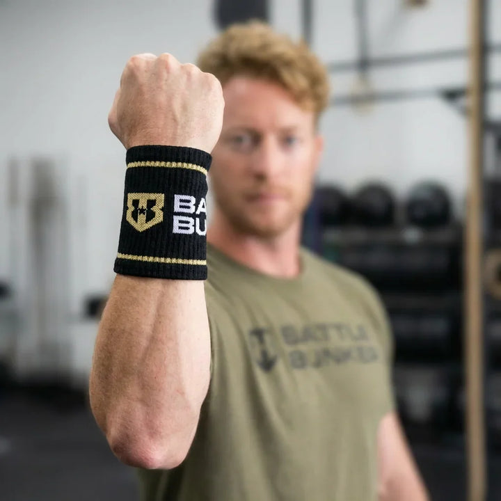 Man wearing black Battle Bunker wrist sweatband with yellow stripes in gym setting