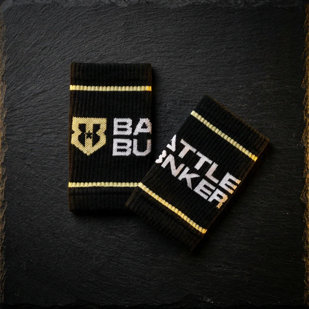 Black Battle Bunker wristbands with gold stripes and logo on dark textured background