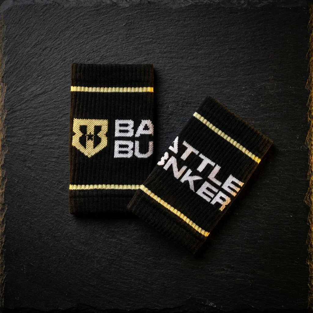 Black Battle Bunker wristbands with gold stripes and logo on dark textured background