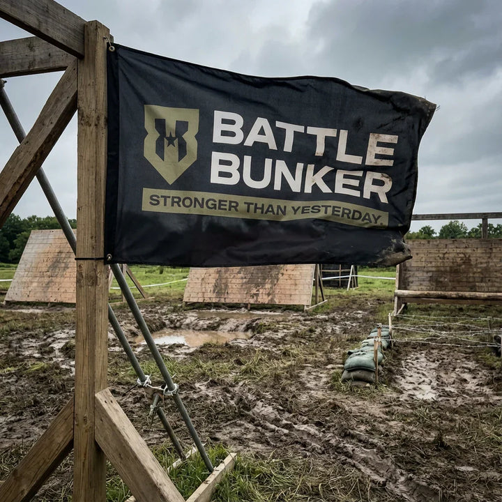 Battle Bunker black banner with logo and slogan at muddy outdoor obstacle course under cloudy sky