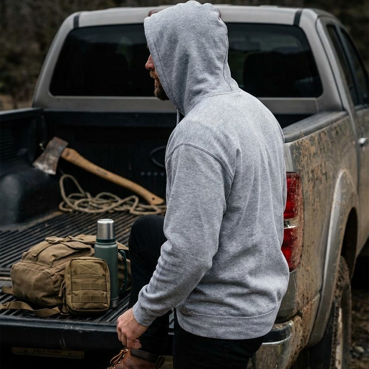 Person wearing a gray hoodie standing next to a pickup truck with camping gear in the back.