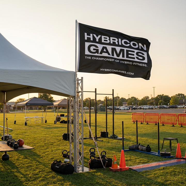 Outdoor fitness event setup with 'Hybricon Games' flag and exercise equipment.