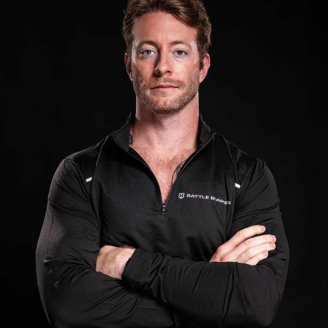 man wearing black Battle Bunker zip-up athletic top with folded arms on black background